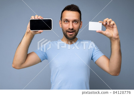 Photo of handsome young unshaven brunet man with beard wearing everyday blue t-shirt isolated over Photo of handsome young unshaven brunet man with beard wearing everyday blue t-shirt isolated over 84128776