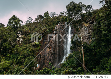 Couple admires a beautiful waterfall. Couple in love at the waterfall. Boy and girl at the falls. A guy and a girl traveling. The couple travels around Asia. Waterfalls in Sri Lanka. Honeymoon trip Couple admires a beautiful waterfall. Couple in love at the waterfall. Boy and girl at the falls. A guy and a girl traveling. The couple travels around Asia. Waterfalls in Sri Lanka. Honeymoon trip 84128917