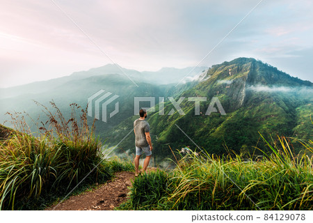 A man stands with his back in the mountains. A man travels in Asia. Travel to Sri Lanka. Traveler in the mountains. A man enjoys a beautiful view of the mountains. Man at sunrise in the mountains 84129078