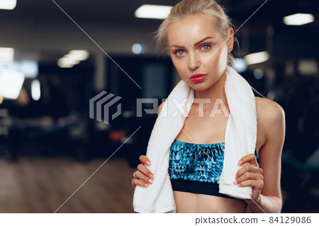 Blonde slim fit woman in sport wear in a dark gym Blonde slim fit woman in sport wear in a dark gym 84129086