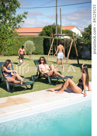 Tranquil female friends sunbathing near swimming pool 84129155
