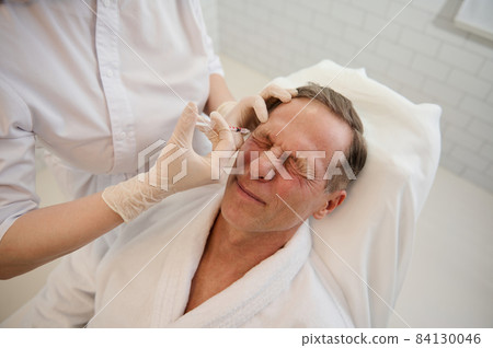 High angle view of a senior European man receiving beauty injection on his face in wellness spa. Mesotherapy, male anti-aging procedure, rejuvenating treatment, professional skin and body care concept High angle view of a senior European man receiving beauty injection on his face in wellness spa. Mesotherapy, male anti-aging procedure, rejuvenating treatment, professional skin and body care concept 84130046