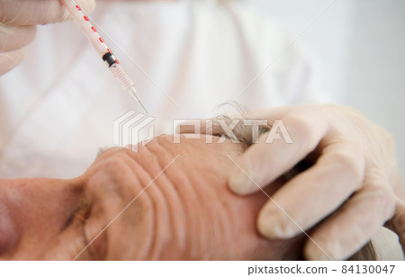 Close-up of aesthetician holding a syringe and making facial injection to handsome aged man in modern spa center. Injection cosmetology, beauty rejuvenating treatment, skin and body care concept 84130047