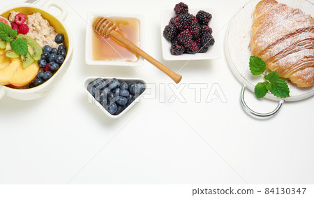 plate with oatmeal and fruit, half a ripe orange and freshly squeezed juice in a transparent glass decanter, honey in a bowl on a white table. Healthy breakfast 84130347
