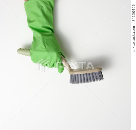 hand in a green rubber cleaning glove holds a plastic brush on a white background hand in a green rubber cleaning glove holds a plastic brush on a white background 84130406