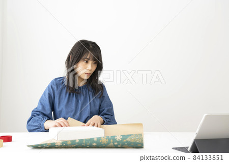 一位年輕女子在辦公桌前打包禮物,同時在互聯網上觀看視頻 一位年輕女子在辦公桌前打包禮物,同時在互聯網上觀看視頻 84133851