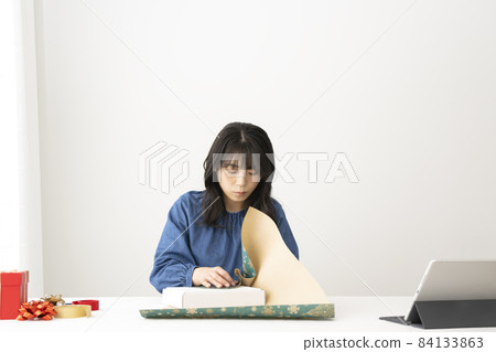 A young woman packing gifts at her desk while watching a video on the internet A young woman packing gifts at her desk while watching a video on the internet 84133863