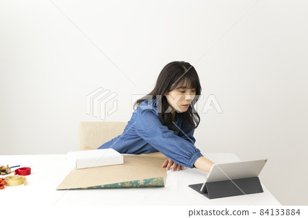 一位年輕女子在辦公桌前打包禮物,同時在互聯網上觀看視頻 一位年輕女子在辦公桌前打包禮物,同時在互聯網上觀看視頻 84133884