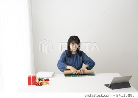 A young woman packing gifts at her desk while watching a video on the internet 84133893