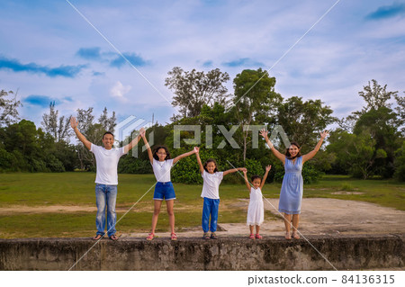 family, leisure and people concept-young active parents with three daughters with arms up, enjoying summer vacation together. Big asian happy family of five. family, leisure and people concept-young active parents with three daughters with arms up, enjoying summer vacation together. Big asian happy family of five. 84136315