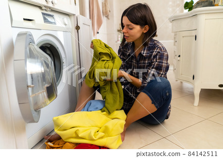 Young girl puts clothes in the washing machine. 84142511