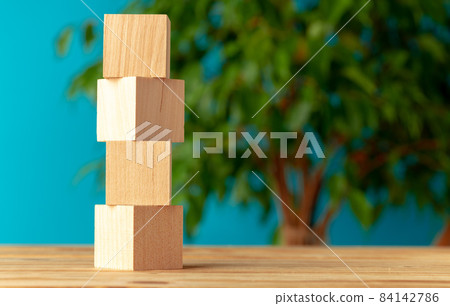 Wooden blocks on desk against blurred plant background Wooden blocks on desk against blurred plant background 84142786