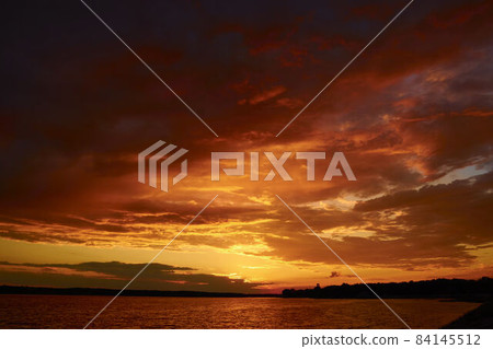 Evening cloudscape in twilight. Ruddy horizon sky and river. Morning fiery orange sunrise in summer dawn. Red cloudy sunset above lake at dusk. Bloody sky above reflective water surface waves in wind Evening cloudscape in twilight. Ruddy horizon sky and river. Morning fiery orange sunrise in summer dawn. Red cloudy sunset above lake at dusk. Bloody sky above reflective water surface waves in wind 84145512
