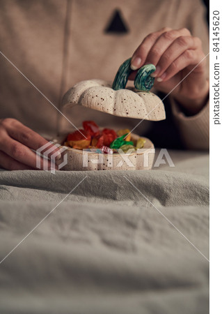 Crop woman opening box with colorful candies 84145620