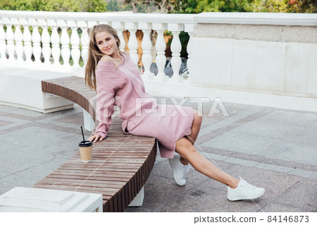 beautiful fashionable blonde woman in pink clothes drinking a coffee cocktail with a straw 84146873