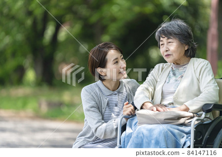 Caregiver and senior woman in a wheelchair talking in the park Caregiver and senior woman in a wheelchair talking in the park 84147116