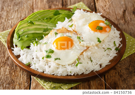 Boiled rice on top with fried eggs served with fresh avocado close-up in a plate. horizontal 84150736