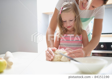 Mom and daughter are kneading dough together in the kitchen 84151190