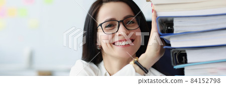 Young woman with glasses holding many folders with documents in office 84152798