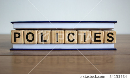 Concept word 'policies' on wooden cubes between pages of a book on a beautiful wooden table. White background. Business concept. 84153584