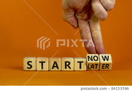 Start now or later symbol. Businessman turns wooden cubes and changes words 'start later' to 'start now'. Beautiful orange background, copy space. Business and start now or later concept. 84153596
