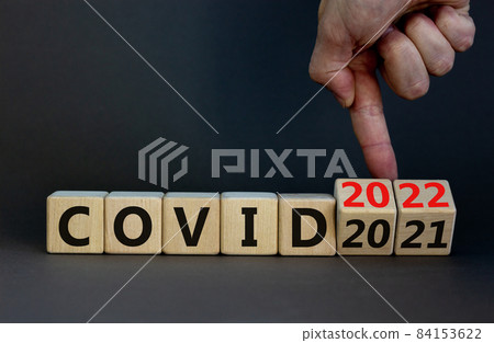 Symbol of covid-19 pandemic in 2022. Doctor turns wooden cubes and changes words 'covid 2021' to 'covid 2022'. Beautiful grey background, copy space. Medical, covid-19 pandemic in 2022 concept. 84153622
