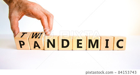 Pandemic or twindemic symbol. Doctor turns wooden cubes and changes the word 'pandemic' to 'twindemic'. Beautiful white background, copy space. Medical and pandemic or twindemic concept. 84153743