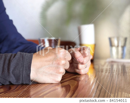 一個女人的手戴著結婚戒指，雙手握拳放在桌子上 84154011