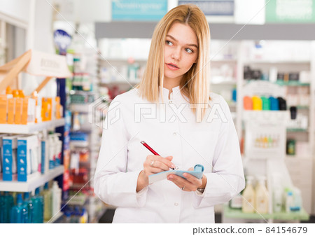 Smiling female pharmacist checking assortment of drugs in pharmacy Smiling female pharmacist checking assortment of drugs in pharmacy 84154679