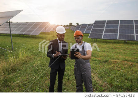 Two multiracial men examining solar panels outdoors 84155438