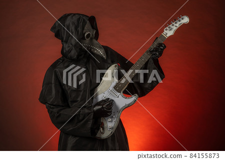 A man in a plague doctor costume plays the guitar emotionally on a red background A man in a plague doctor costume plays the guitar emotionally on a red background 84155873