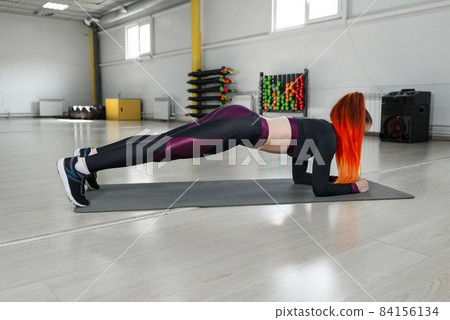 Young athletic woman performing an exercise plank on the floor in the gym. Young athletic woman performing an exercise plank on the floor in the gym. 84156134