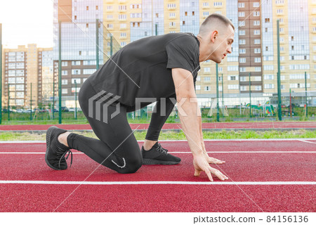 Athlete on the starting line of a stadium track preparing for a run. Athlete on the starting line of a stadium track preparing for a run. 84156136