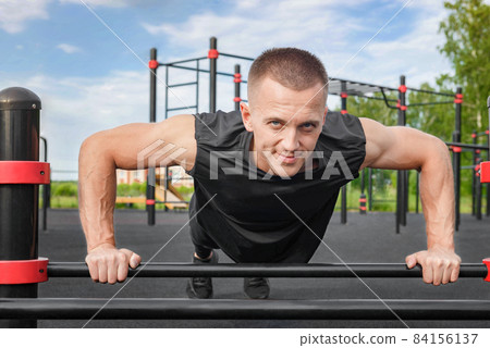 Young man doing push-up exercise on the street on an iron bar. 84156137