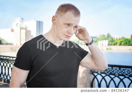Young bearded man in a black t-shirt standing in park and using a smartphone. Young bearded man in a black t-shirt standing in park and using a smartphone. 84156147