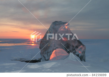Ice of Lake Baikal. Dawn. Winter morning. Nature of Russia. Pink sky. The sun is reflected in a piece of ice Ice of Lake Baikal. Dawn. Winter morning. Nature of Russia. Pink sky. The sun is reflected in a piece of ice 84159899