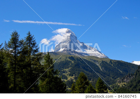 Matterhorn with impressive streaks in the sky, along with green trees and the foot of the mountain Matterhorn with impressive streaks in the sky, along with green trees and the foot of the mountain 84160745