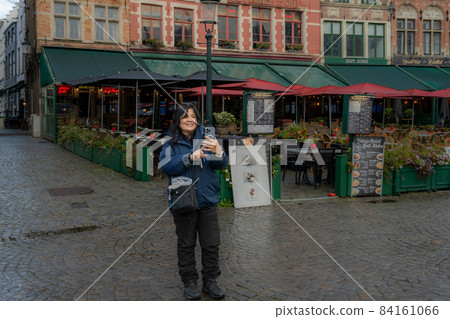 An Asian woman takes a selfie in front of a restaurant. Picture from the market square, Grote Markt, in Bruges, Belgium. An Asian woman takes a selfie in front of a restaurant. Picture from the market square, Grote Markt, in Bruges, Belgium. 84161066