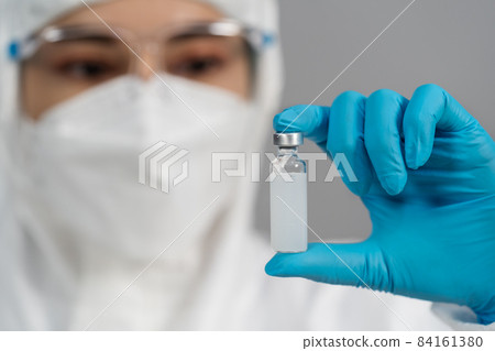 doctor in PPE suit holding and gently shaking vaccine bottle doctor in PPE suit holding and gently shaking vaccine bottle 84161380