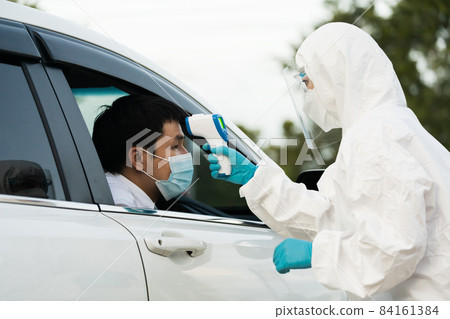 doctor in protective PPE suit using infrared thermometer measuring temperature of man at drive thru station 84161384