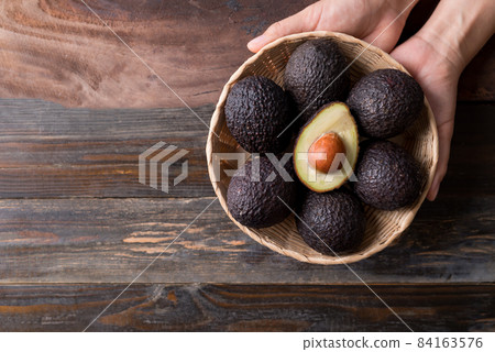 Ripe hass avocado fruit in a basket holding by hand on wooden background 84163576