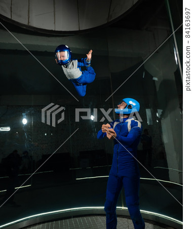 A man teaches a boy to fly in a wind tunnel. 84163697
