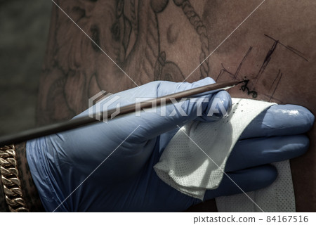 Tattooing concepts. The artist is tattooing a Thai style pattern on the skin with a pointed metal. 84167516