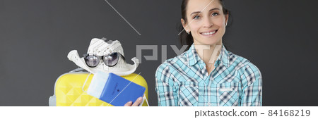 Smiling brunette woman holding passport with ticket and mask next to suitcase 84168219