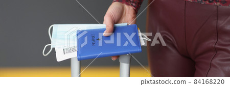 Woman holding passport, plane ticket, medical mask and suitcase Woman holding passport, plane ticket, medical mask and suitcase 84168220