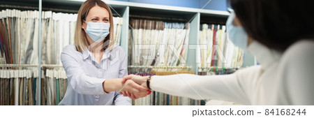 Buyer and seller in protective medical masks shake hands in tissue salon 84168244