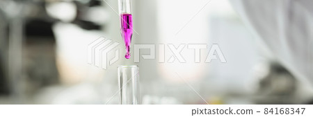 Scientist drops purple liquid from pipette into test tube 84168347