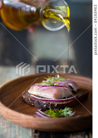 Homemade Borodino rye bread with herring and onions is poured with butter on a wooden bowl. Front view. 84168463