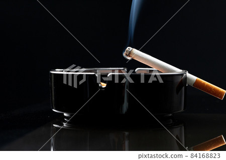 Burning cigarette in a black ash tray 84168823