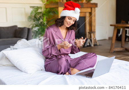 Young woman in Santa hat and pyjama. New normal, quarantine, talking with friends on video call. Celebrating Christmas - online conference chat on notebook at home. Young woman in Santa hat and pyjama. New normal, quarantine, talking with friends on video call. Celebrating Christmas - online conference chat on notebook at home. 84170411